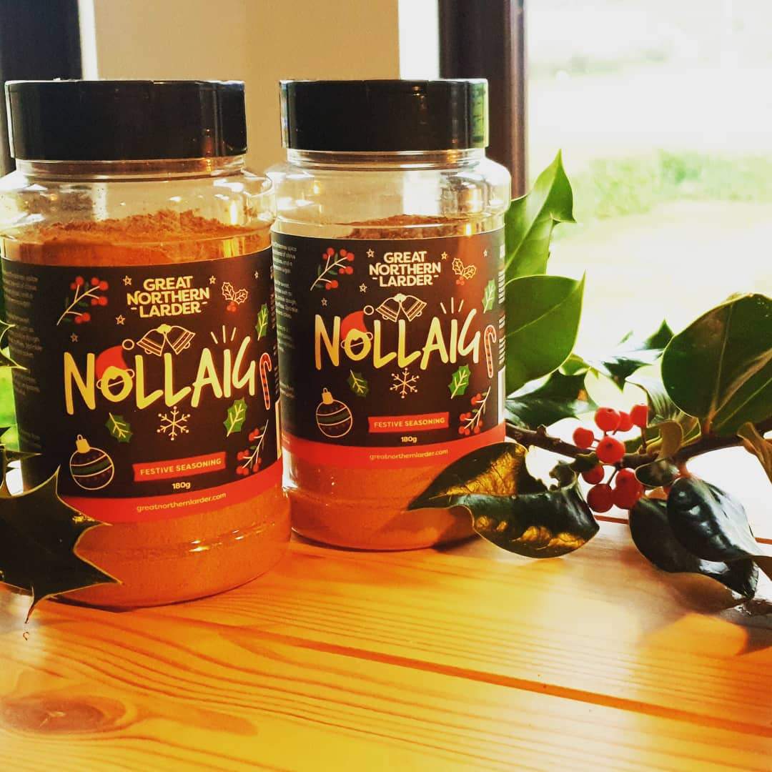 A photograoh of two pots of Nollaig spice rub surrounded by holly and berries.